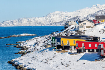 Modern colorful waterfront houses in Nuuk with snowy rocks, deep blue fjord water, distant arctic mountains and clear winter light, Sermersooq, Greenland © vadim.nefedov