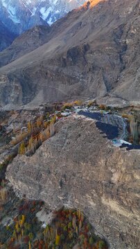 Aerial view of Hunza valley with solar panels on a rocky slope, autumn foliage, and distant snow-capped mountains Hunza Nagar, Gilgit Baltistan, Pakistan.