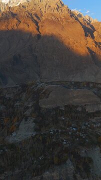 Aerial view of Hunza Valley with golden sunlight hitting the mountain peaks and autumn foliage in the valley below Hunza Nagar, Gilgit Baltistan, Pakistan.