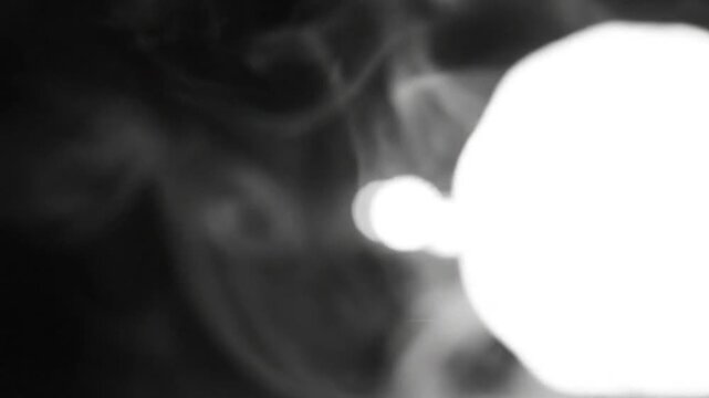 Abstract slow motion video of a bright spherical light surrounded by swirling smoke on a dark background.