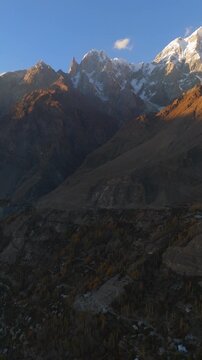 Aerial view of Hunza Valley featuring snow-capped mountain peaks and autumn foliage on rocky slopes in Hunza Nagar, Gilgit Baltistan, Pakistan.
