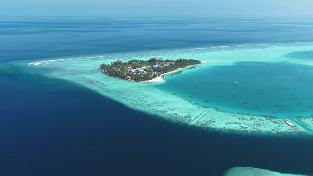 Aerial view of a lush tropical island surrounded by turquoise coral reefs and deep blue ocean waters in Kudahuvadhoo, Dhaalu Atoll, Maldives.