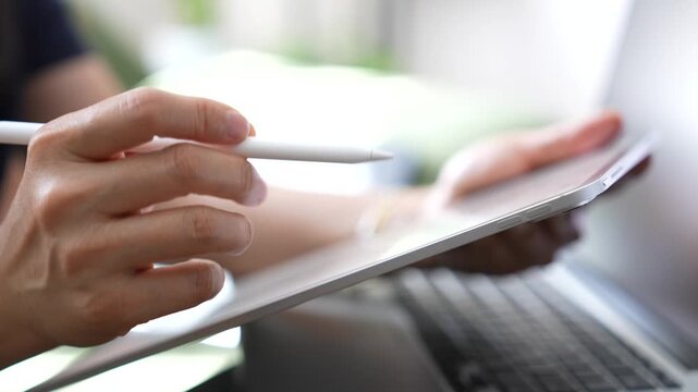 Person using tablet with stylus beside laptop for digital note taking, online workflow, electronic signature, document management, remote work, business productivity, modern technology.
