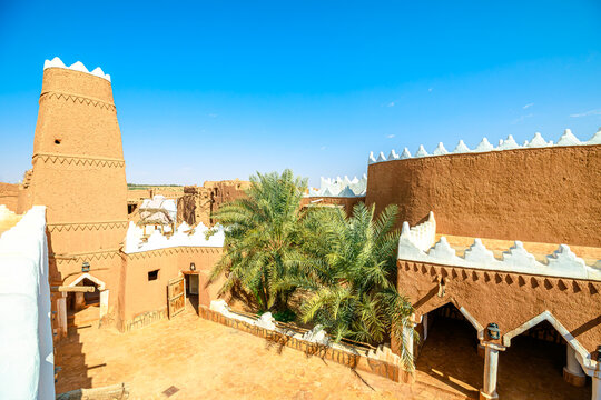 Ushaiqer Heritage Village entrance with a weathered wooden door and traditional lock opening to a courtyard of mud-brick walls, and a distinctive support pillar in Najdi style of Saudi Arabia