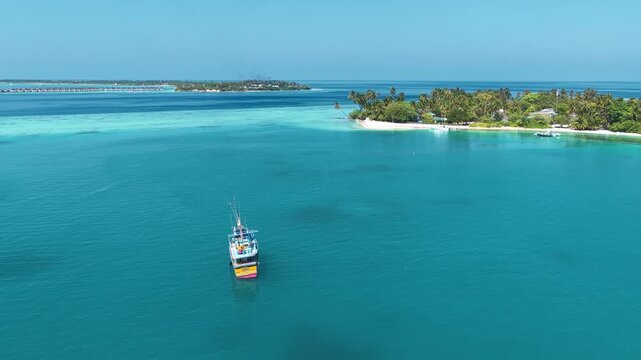 Aerial view of a Sri Lankan boat floating on the turquoise sea near a tropical island with palm trees and white sand beaches in Kudahuvadhoo, Dhaalu Atoll, Maldives.
