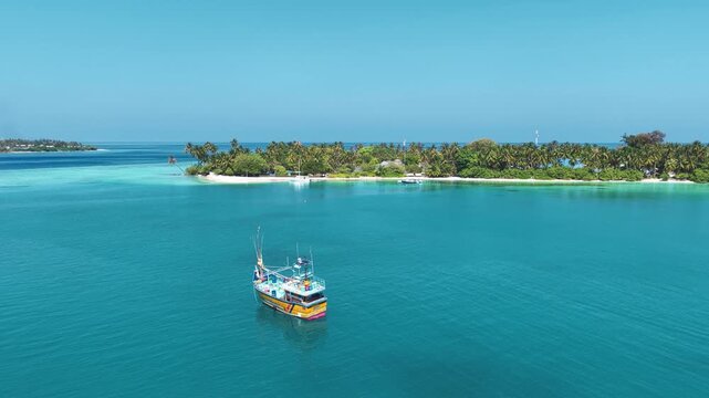 Aerial view of a fishing boat floating on turquoise water near a tropical island with palm trees in Kudahuvadhoo, Dhaalu Atoll, Maldives.