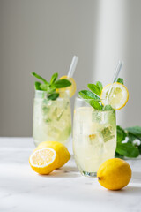 Fototapeta premium A refreshing summer drink with lemon, mint, and ice in a two glasses on a light background.