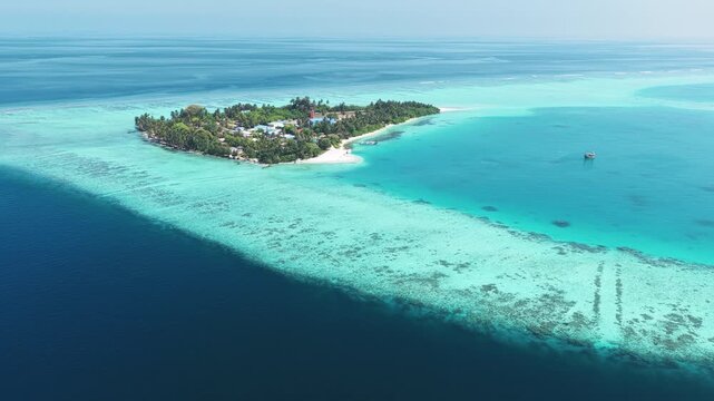 Aerial view of a lush tropical island surrounded by turquoise coral reefs and deep blue ocean waters in Kudahuvadhoo, Dhaalu Atoll, Maldives.