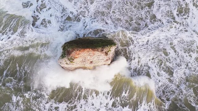 Aerial drone top down view of  Stag Rock at Freshwater Bay, Isle of Wight, showing waves crashing against cliffs and rocky shoreline on a cloudy winter day.