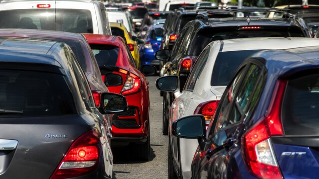 A heavy traffic jam with multiple vehicles stopped on a multilane highway, displaying bright red brake lights during a daytime congested commute
