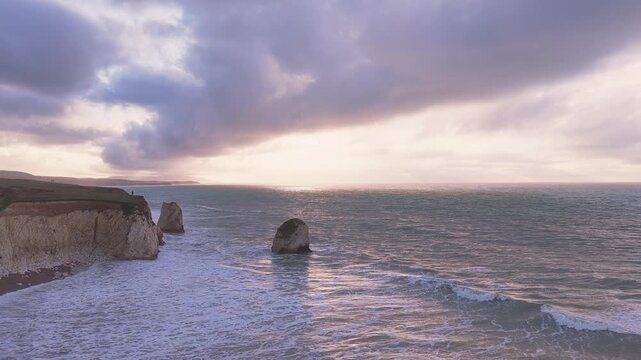 Drone flyover of Stag Rock and chalk cliffs at Freshwater Bay, coastal headland and crashing waves, Isle of Wight