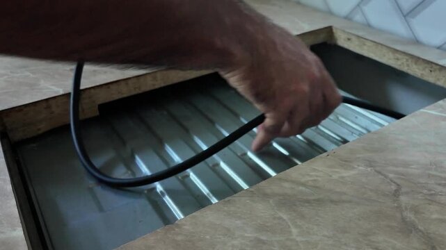 A hand installing a hob into a countertop. The countertop is made of wooden with a cutout for the hob. Tools and wires are visible nearby.