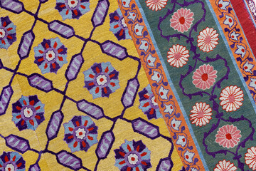 Fototapeta premium Vibrant woven rug featuring intricate floral motifs and geometric lattice on bold yellow and green bands. Ornate decorative textile evokes traditional craftsmanship