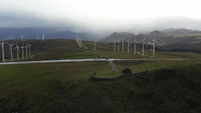 Aerial view of the Garita de Herbeira stone hut and a wind farm on the misty hills under an overcast sky in Meizoso, A Coruna, Spain.