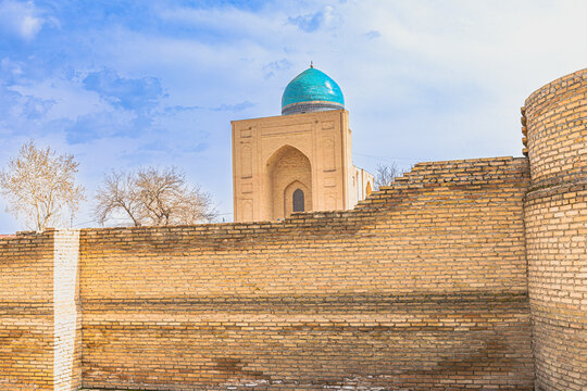 Long view of a tall protective brick wall enclosing a turquoise-domed historical building in Samarkand, Uzbekistan. Bibi Khanym brick mausoleum with a blue turquoise
