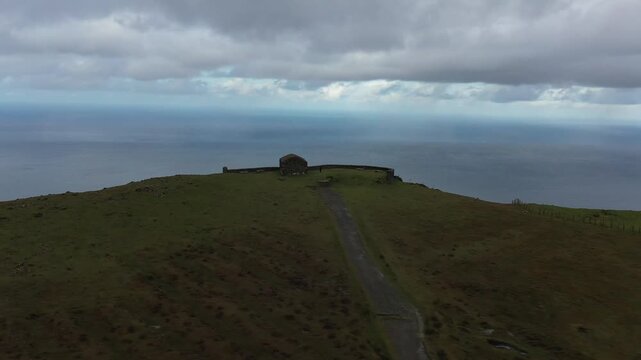 Aerial view of Garita de Herbeira stone hut on the high cliffs overlooking the Atlantic Ocean under a cloudy sky in Meizoso, A Coruna, Spain.
