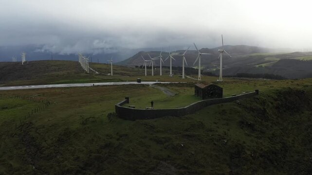 Aerial view of the historic Garita de Herbeira stone guardhouse and a row of wind turbines on a misty ridge in Meizoso, A Coruna, Spain.