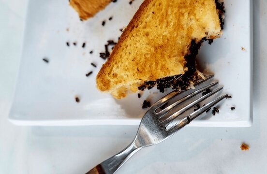 Close up of half eaten grilled toast bread with chocolate sprinkles or meses on white plate with fork. Indonesian street food breakfast snack concept.