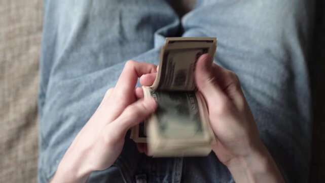 A man counts a stack of cash with both hands. The cash is arranged neatly in his hands, highlighting the green money and his focused expression.