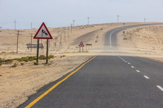 Sand being blown over the road to Luderitz, Namibia, with various warning and direction signs, including one for strong winds.