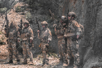 Fototapeta premium Professional tactical team standing in defensive line against rugged mountain cliff. Elite soldiers in combat gear maintaining high alert during field operation, military training or security mission.