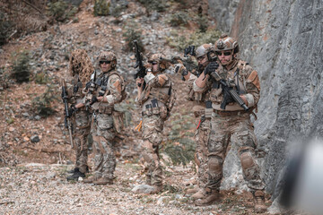 Fototapeta premium Professional tactical team standing in defensive line against rugged mountain cliff. Elite soldiers in combat gear maintaining high alert during field operation, military training or security mission.