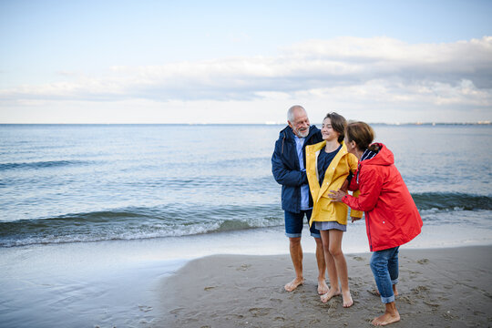 Grandparents walking with teenage granddaughter on beach during family vacation.