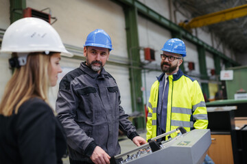 Fototapeta premium Manager supervisors and industrial worker in uniform walking in large metal factory hall and talking. Low angle view.