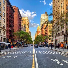 Fototapeta premium A city street with tall buildings on both sides, lined with trees and featuring cars on the road