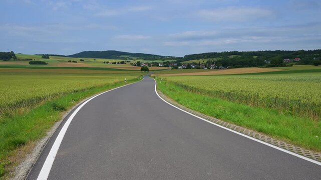 Eine gewundene Landstra&szlig;e f&uuml;hrt durch eine l&auml;ndliche Landschaft mit H&uuml;geln und Wiesen und kleinen Ort, Orferode, Stadt Bad Sooden-Allendorf, Werra-Mei&szlig;ner-Kreis, Hessen, Deutschland
