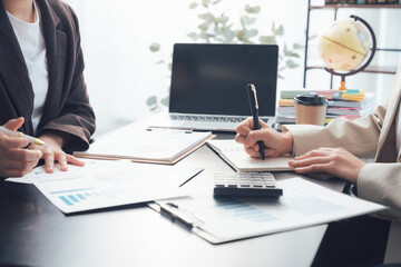 Obraz premium Business Meeting in Progress: Two individuals engaged in a focused discussion over documents and charts at a table, with a laptop and office supplies in the background.