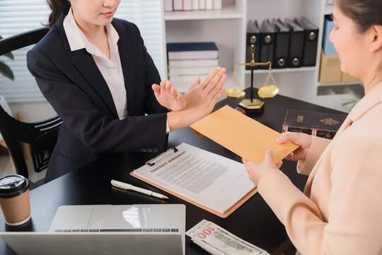 A hand in a suit pushes away an envelope offered by another person, symbolizing refusal of a bribe in a professional setting.
