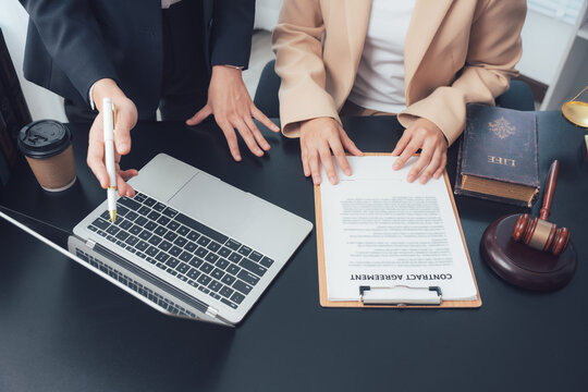 Legal Consultation: Two individuals are reviewing a contract at a desk, with a laptop, gavel, and law book in view, signifying a legal discussion and contract agreement.