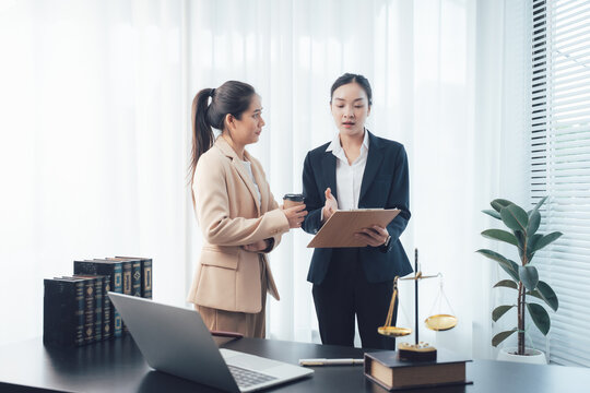 Legal Consultation: Two professional women, likely lawyers or paralegals, are engaged in a serious discussion in an office setting.