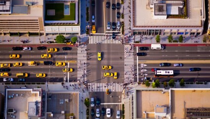 Overhead aerial view of a busy urban intersection with a strong tilt-shift miniature effect, rows of yellow taxis queuing at crosswalks giving a toy-like appearance from above. © olga_demina