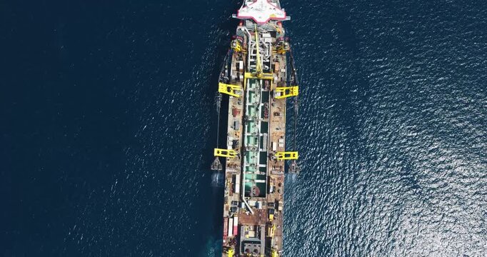 Aerial view of an industrial barge with yellow cranes navigating the deep blue ocean waters near Dhidhdhoo, Haa Alif Atoll, Maldives.