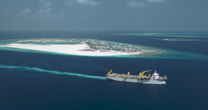 Aerial view of a large industrial ship sailing through deep blue waters near the tropical island of Dhidhdhoo, Haa Alif Atoll, Maldives.