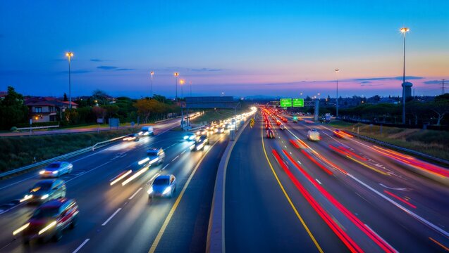 Long-exposure dusk shot of a multi-lane freeway at blue hour with bright headlight and red tail-light streaks flowing beneath illuminated green highway signs and glowing street lamps.