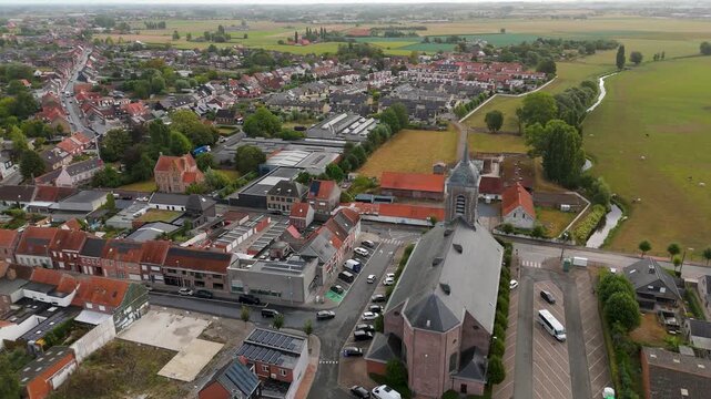 Drone view capturing the historic Saint Peter church next to green agricultural fields and town houses in Ledegem, West Flanders.