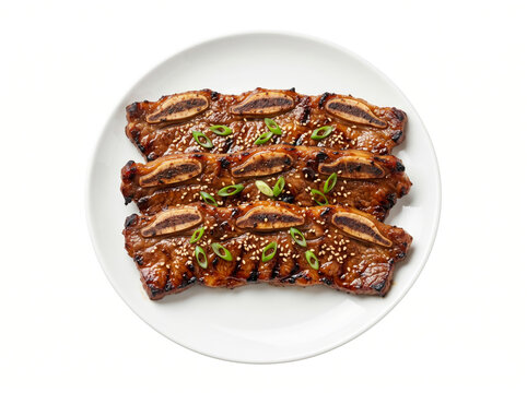 Grilled Korean galbi short ribs on a white plate, marinated, caramelized, garnished with sesame seeds and scallion slices.