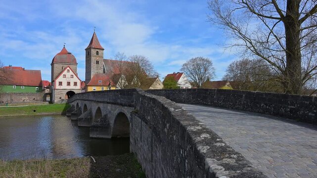 Steinbr&uuml;cke &uuml;ber einen Fluss zu einem Dorf mit einer Kirche und historischen Geb&auml;uden unter blauem Himmel, Fr&uuml;hling, Ornbau, Triesdorf, Fr&auml;nkischen Seenland, Landkreis Ansbach, Mittelfranken, Bayern, 