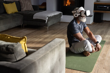 Obraz premium Senior African American man sitting on green yoga mat at home wearing VR headset, copy space