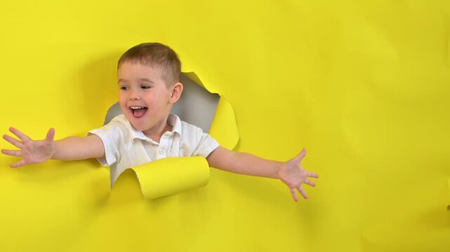 A mischievous boy peeks out through a hole in a yellow cardboard background. 
