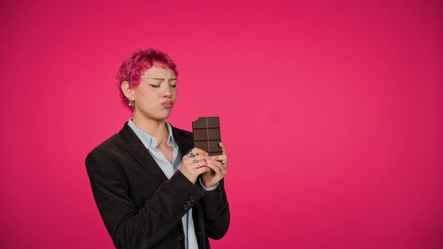 Young person with pink hair eating dark chocolate bar