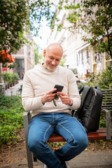 Fototapeta premium Mature man using smartphone while sitting on park bench in city