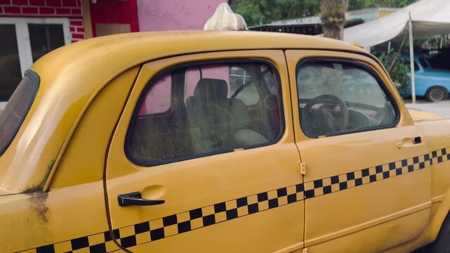 Classic yellow taxi car with checkerboard stripe parked outdoors on a sunny day