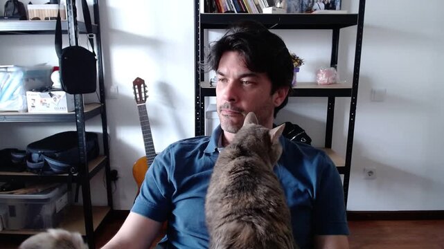 Man with cat tail obscuring face in home office with guitar and shelves
