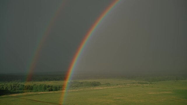 Vivid double rainbow arching across a stormy sky above a lush green countryside meadow after a rain shower, creating an exceptional and colorful atmospheric optical phenomenon