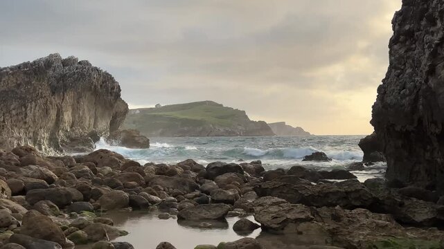 Rocky coastal passage opening toward the Atlantic ocean with moving waves, layered cliffs and soft evening light along a rugged shoreline.