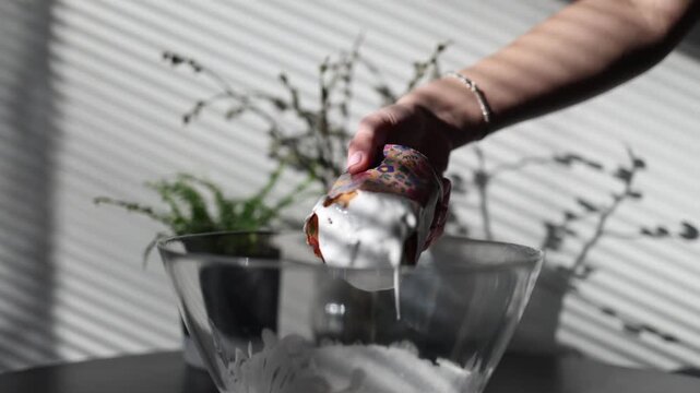 Woman dips traditional easter bread into smooth white icing preparing festive homemade pastry decoration during seasonal holiday baking in a cozy kitchen